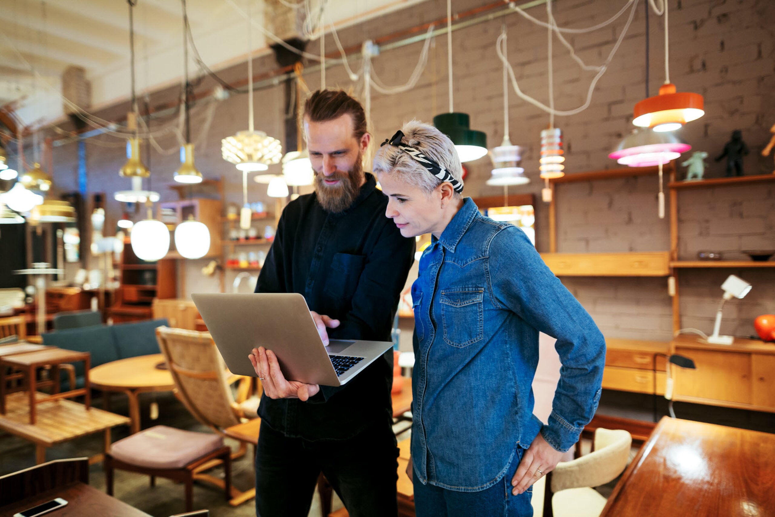 Man and woman in a lighting store, looking at a laptop while discussing Small Business Restructuring (SBR) for addressing excessive tax debt.
